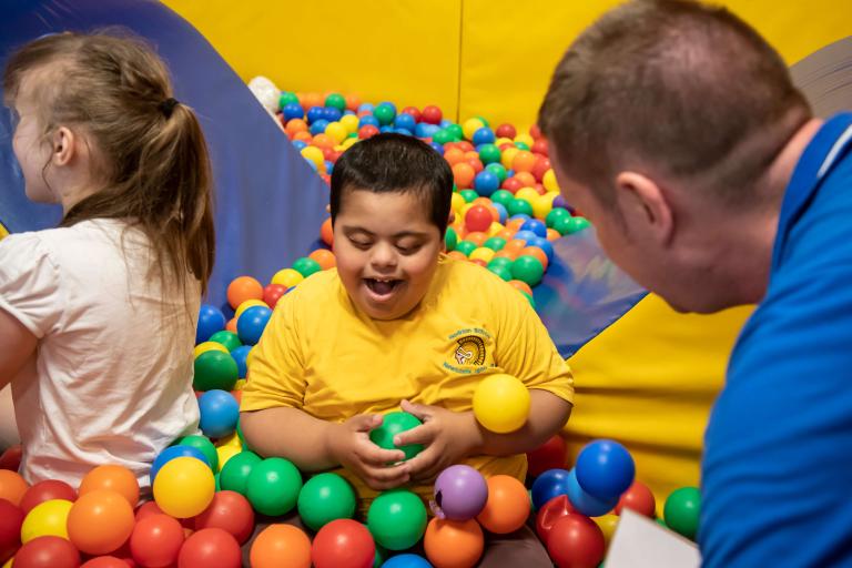 Two young people, supported by an adult playing in a ball pool
