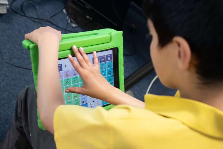 A boy in a yellow school polo shirt holds a green tablet with different coloured squares.