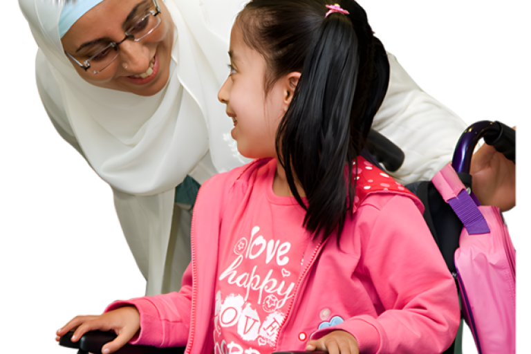 Woman in headscarf smiling at a girl in a wheelchair wearing a pink jacket.