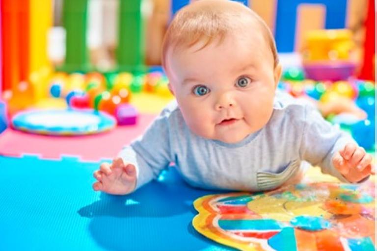 Baby lying on its tummy in a colourful play area.