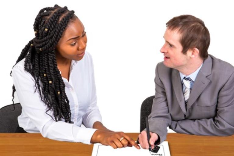 Two people wearing work clothes filling out a form together.