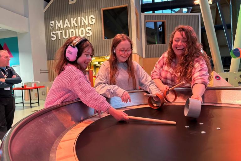 Two smiling girls, one of them with ear defenders, and a women at Life Science Centre