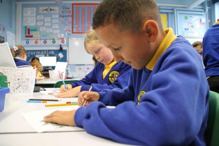 Two primary school students in a classroom holding pencils completing school work.