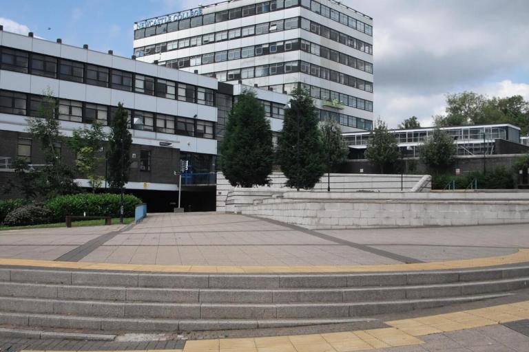 A tall Newcastle College building with a large paved area in front.