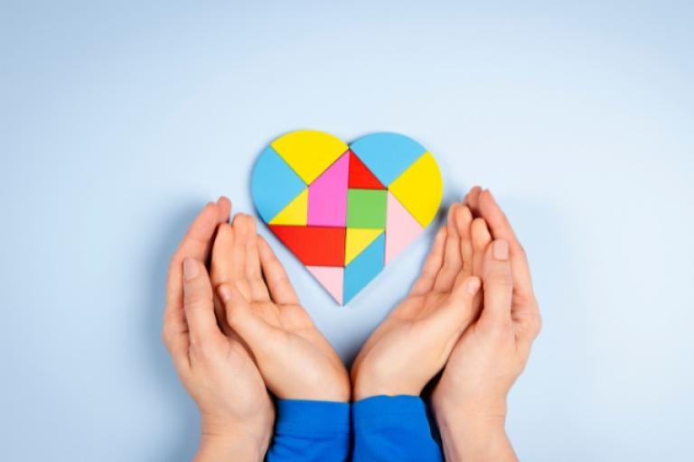 Adult and child's hands cradling below a colourful heart shaped jigsaw