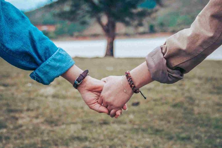 Two people holding hands in front of a tree