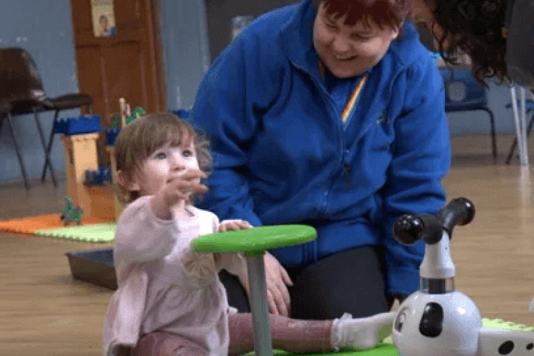A smiling adult with a toddler sat in a room filled with toys