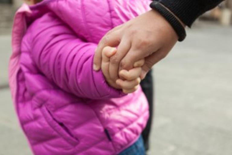 Young child in puffy coat holding the hand of an adult