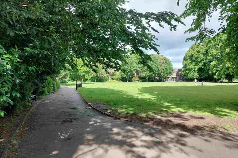 A wide path, field, and trees on a sunny day at Gosforth Central Park.