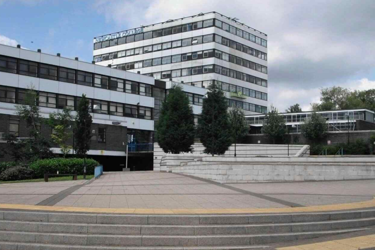 A tall Newcastle College building with a large paved area in front. 
