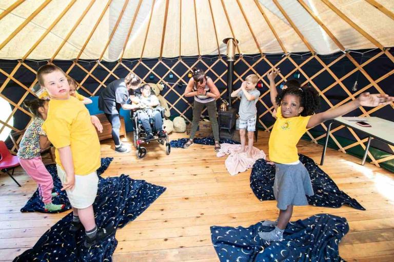 A group of children standing on space themed blankets in a large bright tent.