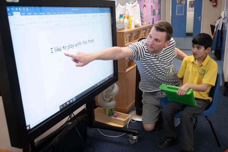 A man next to a boy in a yellow school polo shirt points at words on an interactive whiteboard