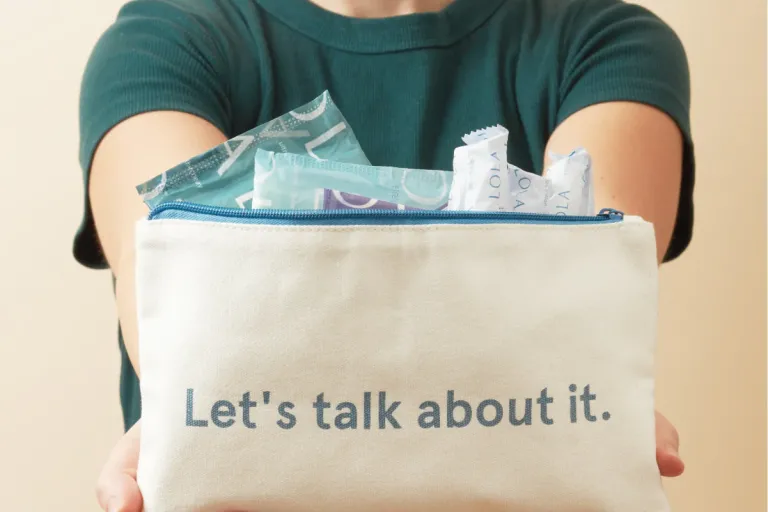Person holding a small pouch containing period products that has writing on which says 'let's talk about it'