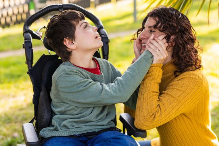 Child in wheelchair holding face of adult crouched next to him