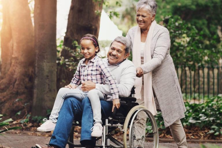 Grandmother pushing grandfather in a wheelchair.  Small child sitting on his knee.