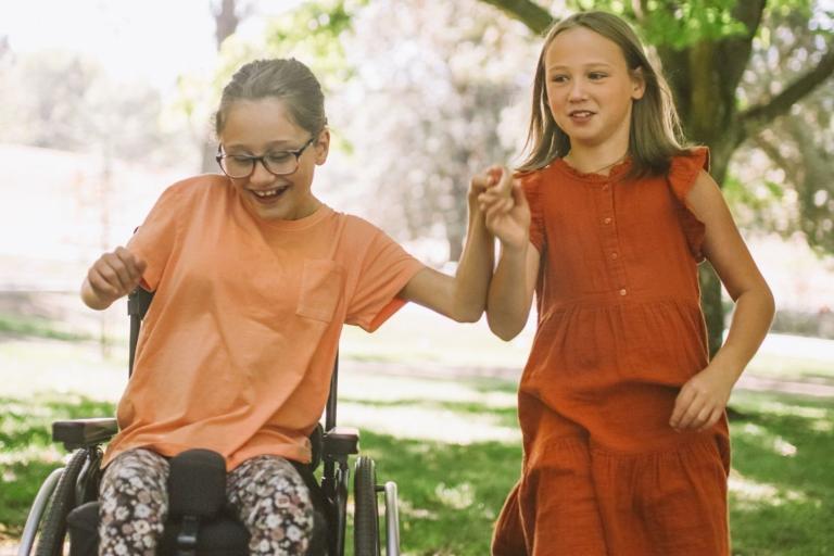 Child in wheelchair holding hands with child walking alongside