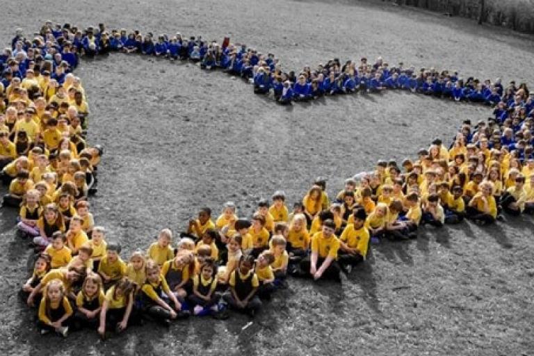 primary school students sitting together in a field and placed to make the shape of a heart