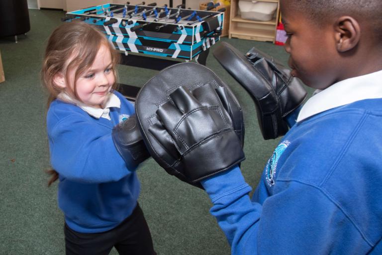 A young girl in boxing gloves sparing thing young boy with table football table in the background