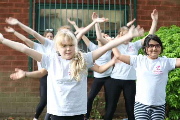 Group of girls with arms raised in a dance performance outdoors. 