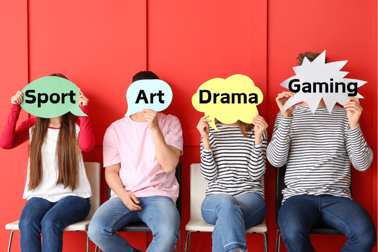 Four young people sitting in a row on chairs, each holding a speech bubble in front of their face one saying sport, one saying art, one saying drama and one saying gaming. 