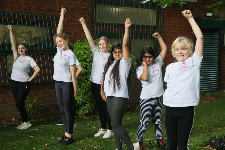 a group of young people outside a building all with one hand raised in the air. 