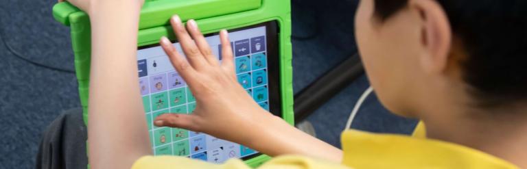 A boy in a yellow school polo shirt holds a green tablet with different coloured squares.