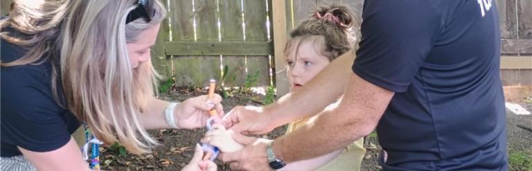 Two adults helping a young girl prepare her toy nerf gun