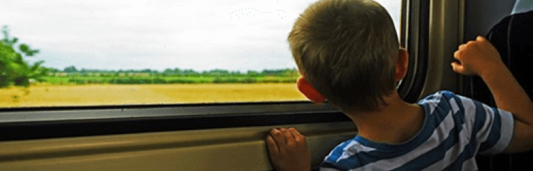 Child looking at a yellow field outside the window of a moving train 