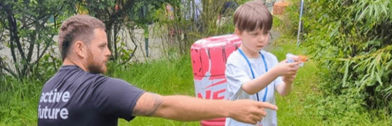 Boy standing outside aiming a nerf gun as an adult points to where he should aim