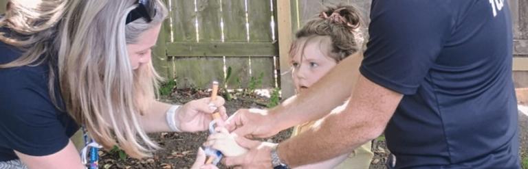 Two adults helping a young girl prepare her toy nerf gun