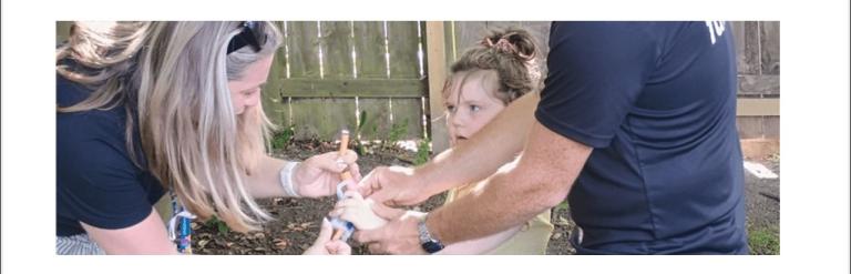 Two adults helping a young girl prepare her toy nerf gun