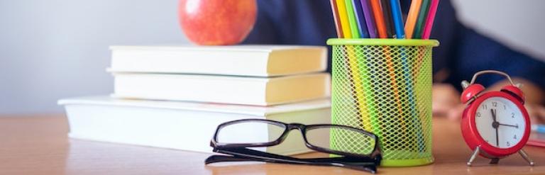 Child sat behind school related items including books, pencils and an apple